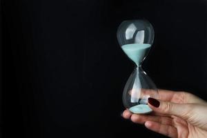 Female hand holding hourglass on black background. photo