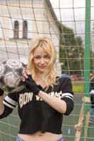 hermosa rubia con una pelota en la portería de fútbol. foto