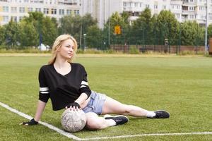 The girl is sitting on the football field with the ball. photo