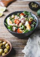Canned tuna salad with fresh vegetables, capers and olives in a black bowl photo