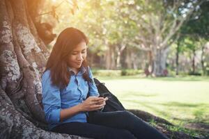 Young hipster woman typing on her phone while sitting at green park. photo