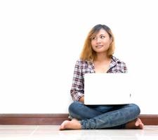 Happy young woman sitting on the floor with crossed legs and using laptop. photo