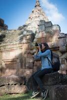 Young attractive woman photographer tourist with backpack coming to shoot photo at ancient phanom rung temple in thailand.