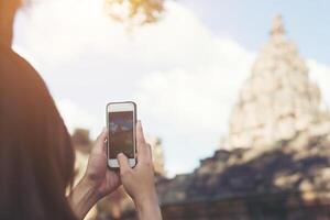 joven y atractiva mujer fotógrafa turista con mochila que viene a tomar una foto con su teléfono inteligente en el antiguo templo de peldaño fantasma en tailandia.