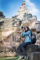 Young attractive woman photographer tourist with backpack coming to shoot photo at ancient phanom rung temple in thailand.