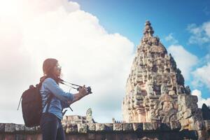 Young attractive woman photographer tourist with backpack coming to shoot photo at ancient phanom rung temple in thailand.