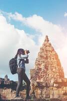 Young attractive woman photographer tourist with backpack coming to shoot photo at ancient phanom rung temple in thailand.