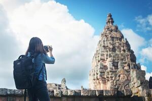 Young attractive woman photographer tourist with backpack coming to shoot photo at ancient phanom rung temple in thailand.