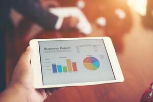 Business person hand holding financial statistics displayed on the tablet screen at office. photo