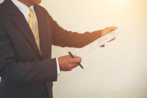 Businessman standing analyzing investment charts with pen in hand at office. photo