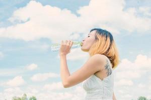 concepto de estilo de vida de las mujeres mujer hermosa joven con vestido blanco bebiendo agua en el parque verde de verano.