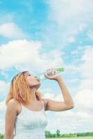 Women lifestyle concept  young beautiful woman with white dress drinking water at summer green park. photo