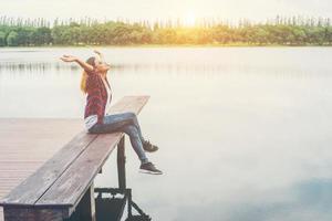Young hipster woman sitting on pier raised hands,relaxing with natural freedom,enjoy and happy.