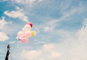 un joven hipster feliz sosteniendo globos de colores en los pastizales disfruta de la vida y es feliz. foto