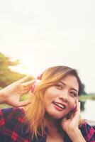 Portrait of young hipster woman with headphones sitting on pier and listening music relaxing with sunset,Lifestyle concept. photo