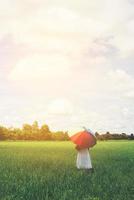 Back Of Young Beautiful woman holding multicolored umbrella in green grassland field and cloud blue sky. photo