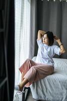 A woman in a white shirt sitting on the bed and raising both arms. photo