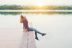 joven hipster sentada en un muelle de madera, relajando la pierna acostada hasta el lago. foto