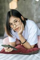 mujer vestida con una camisa blanca acostada en la cama y jugando smartphone. foto