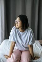 A woman in a white shirt sitting on the bed and looking out. photo