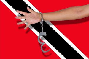 handcuffs with hand on Trinidad and Tobagoh flag photo