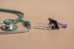 Graduation cap with stethoscope and numbers 2022 on beige background, closeup with copy space. Medical education concept. photo