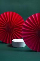 White podium or pedestal with decorative red paper fans on a green background. Product presentation concept. copy space photo