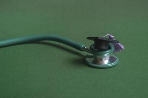 Graduation cap with stethoscope on green background, closeup with copy space. Medical education concept. photo