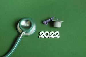 Graduation cap with stethoscope and numbers 2022 on green background, closeup with copy space. Medical education concept. photo