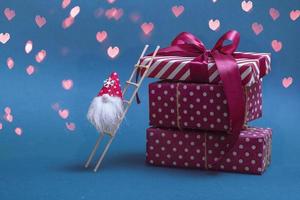 Postcard layout. Heap of gifts on a blue background with bokeh in the form of a heart and a gnome on the stairs. With copy space closeup photo