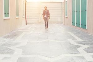 Young hipster man walking on urban street with backpack on his shoulder, to adventure. photo