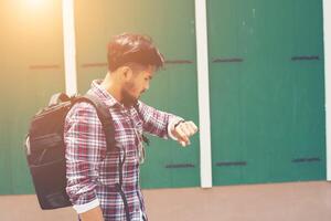 Young man looking at his hand-watch before go to travel with backpack on his shoulder. photo