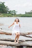 mujer joven sentada estira sus manos sobre el tronco de un árbol en el lago y sonriendo. foto