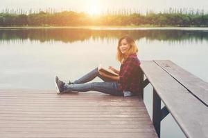 young beautiful hipster woman relaxing sitting on pier reading book, smile to camera.