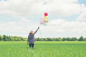 Back of young hipster asian woman with colored balloons in grass field. photo