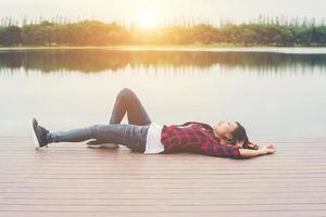 Happy young hipster woman lay down at the pier lake,relaxing enjoy with nature.
