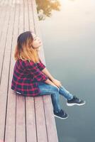 Happy young hipster woman sitting at the pier lake,relaxing enjoy with nature. photo