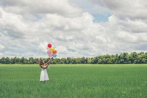 Happy young beautiful woman holding balloons in the grass field enjoy with fresh air. photo