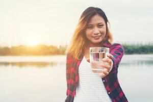 joven y bella mujer hipster sosteniendo agua parada en el muelle, sonriendo a la cámara. foto