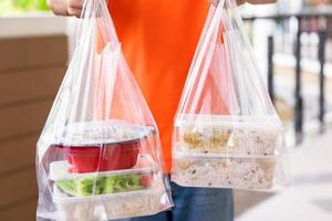 Asian food boxes in plastic bags delivered to customer at home by delivery man in orange uniform photo