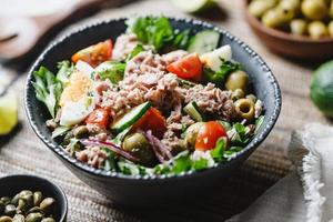 Ensalada de atún enlatado con verduras frescas, alcaparras y aceitunas en un bol negro. almuerzo o cena saludable.