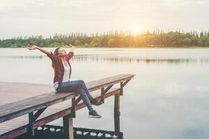 joven hipster sentada en el muelle levantó las manos, relajándose con libertad natural, disfrutando y feliz. foto