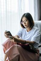 A woman wearing a white shirt, sitting on the bed and playing a smartphone. photo