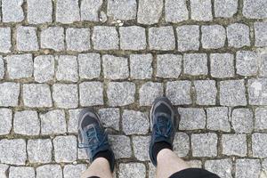 Top view of the feet on the cobblestones in sneakers. photo