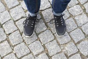 Top view of the feet on the cobblestones in sneakers. photo