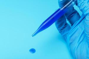 A gloved hand holding a laboratory pipette with blue liquid. photo