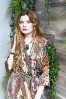 A beautiful girl with red curly hair stands against a wooden wall. photo