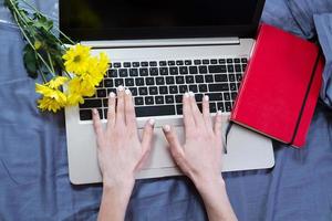 Work space at home, keyboard top view, female hand close up, notebook, work space on bed top view, flowers, colour background photo