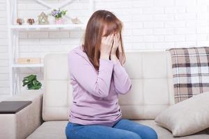 Beautiful middle aged brunette woman crying on sofa. Home background. Menopause time. Copy space and mock up photo