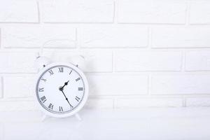 White retro alarm clock near brick wall on white workplace. Selective focus and copy space photo